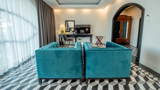 A hotel room with a black and white checkered floor, a desk with a chair, a television, and two teal sofas. - Hotel 1925 (Lipa)