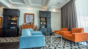 Una sala de estar con sofás azules, un sillón naranja, armarios de madera oscura y un suelo estampado.