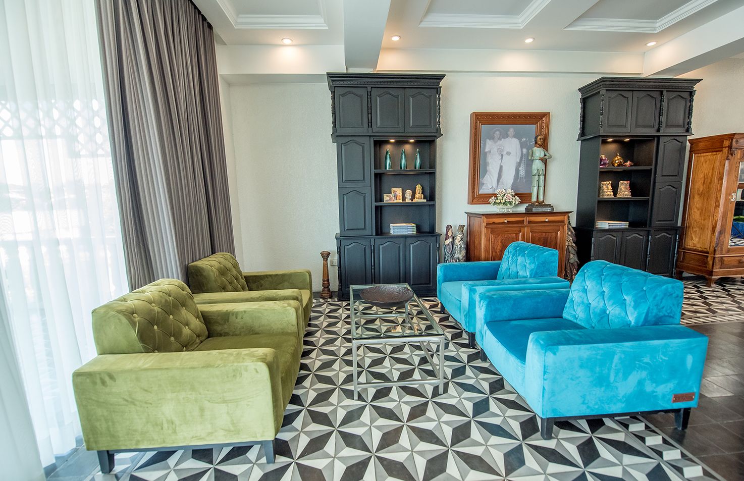Una sala de estar con dos sofás verde y dos azules, una mesa de centro y un piso estampado.
