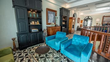 Un salón amplio con suelo de estampado geométrico, un conjunto de sofá azul, armarios de madera oscura y una escalera que sube a otro nivel.