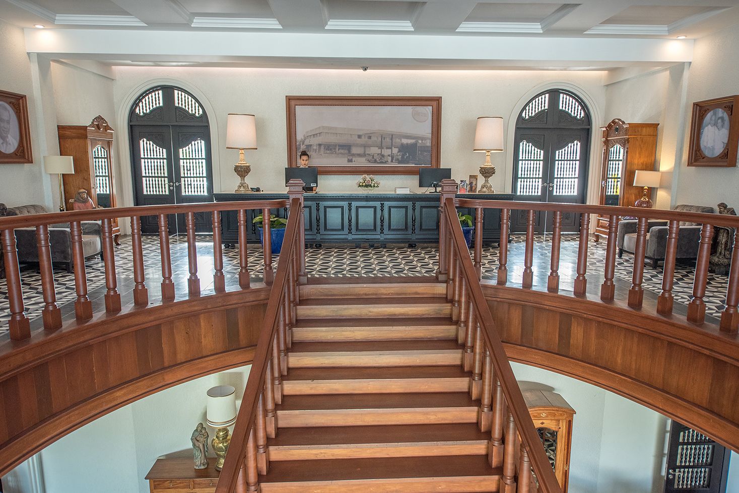 A grand staircase with a wooden railing leading to a dining area with a high ceiling and decorative lighting.