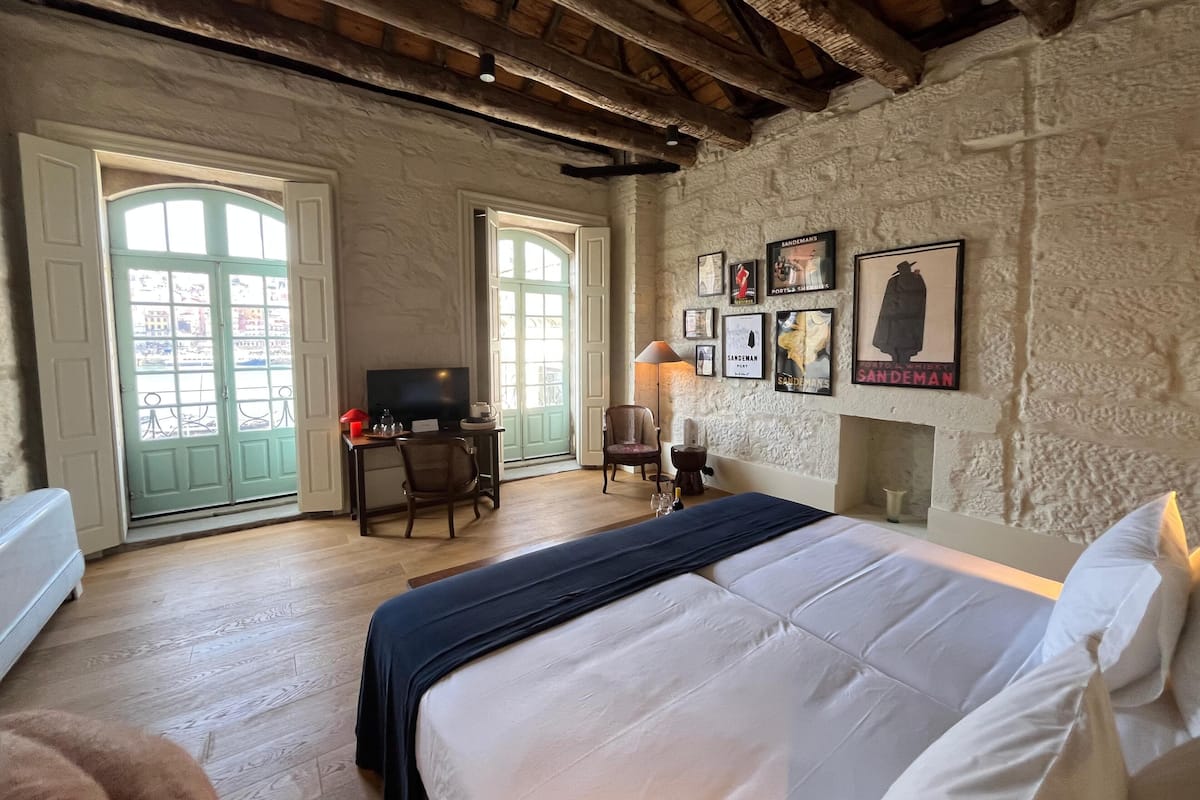 Une chambre avec un grand lit, un bureau avec une chaise, une télévision et une cheminée. Deux portes donnent sur un balcon.