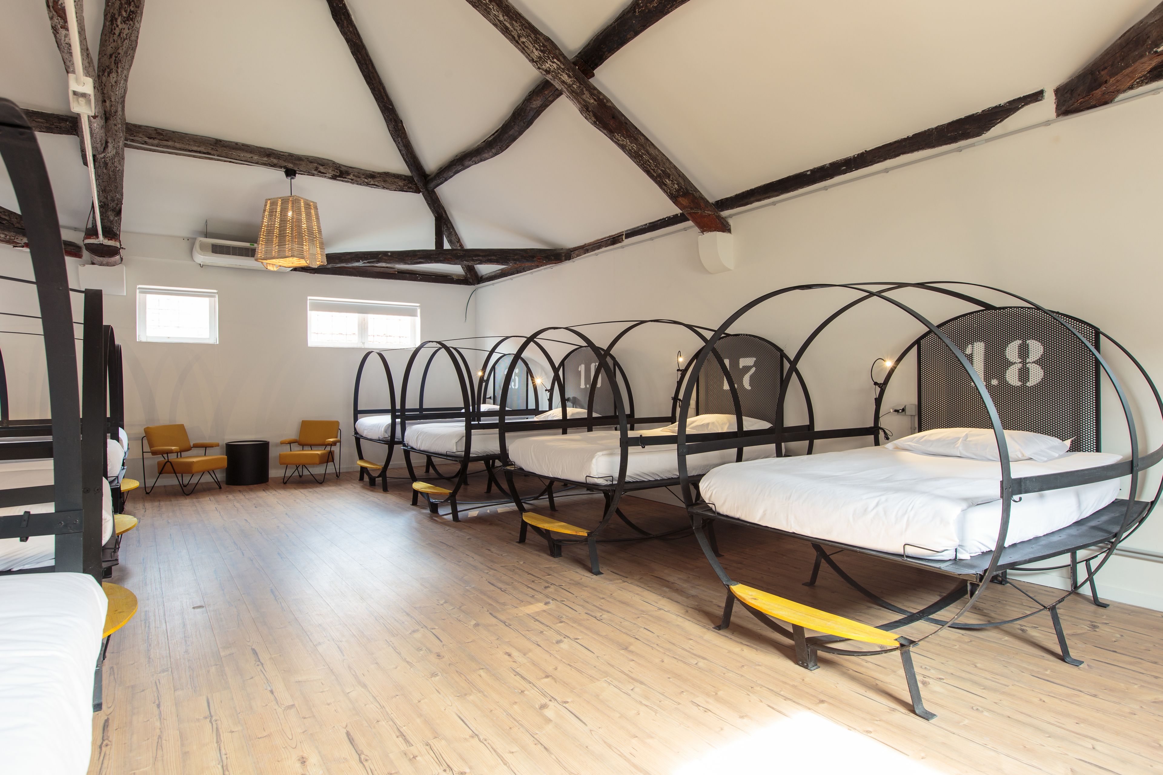 Quarto com quatro camas redondas, piso de madeira e teto inclinado com vigas aparentes.