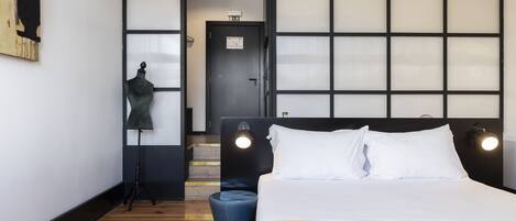 Ett hotellrum med en stor säng, en garderob, en liten pall och en skylldocka.