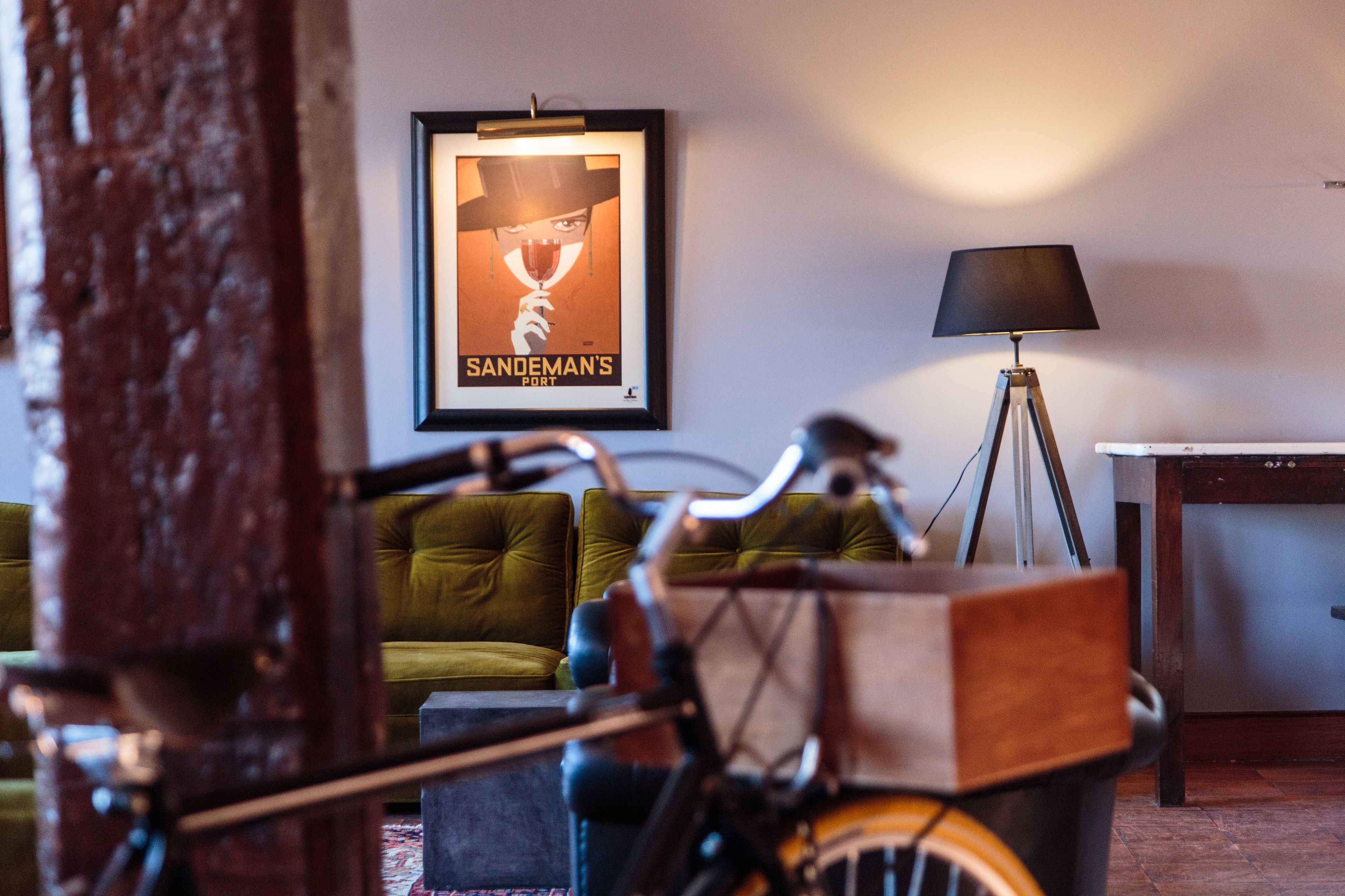 Une pièce avec un canapé vert, une affiche encadrée, une lampe sur pied et un vélo.