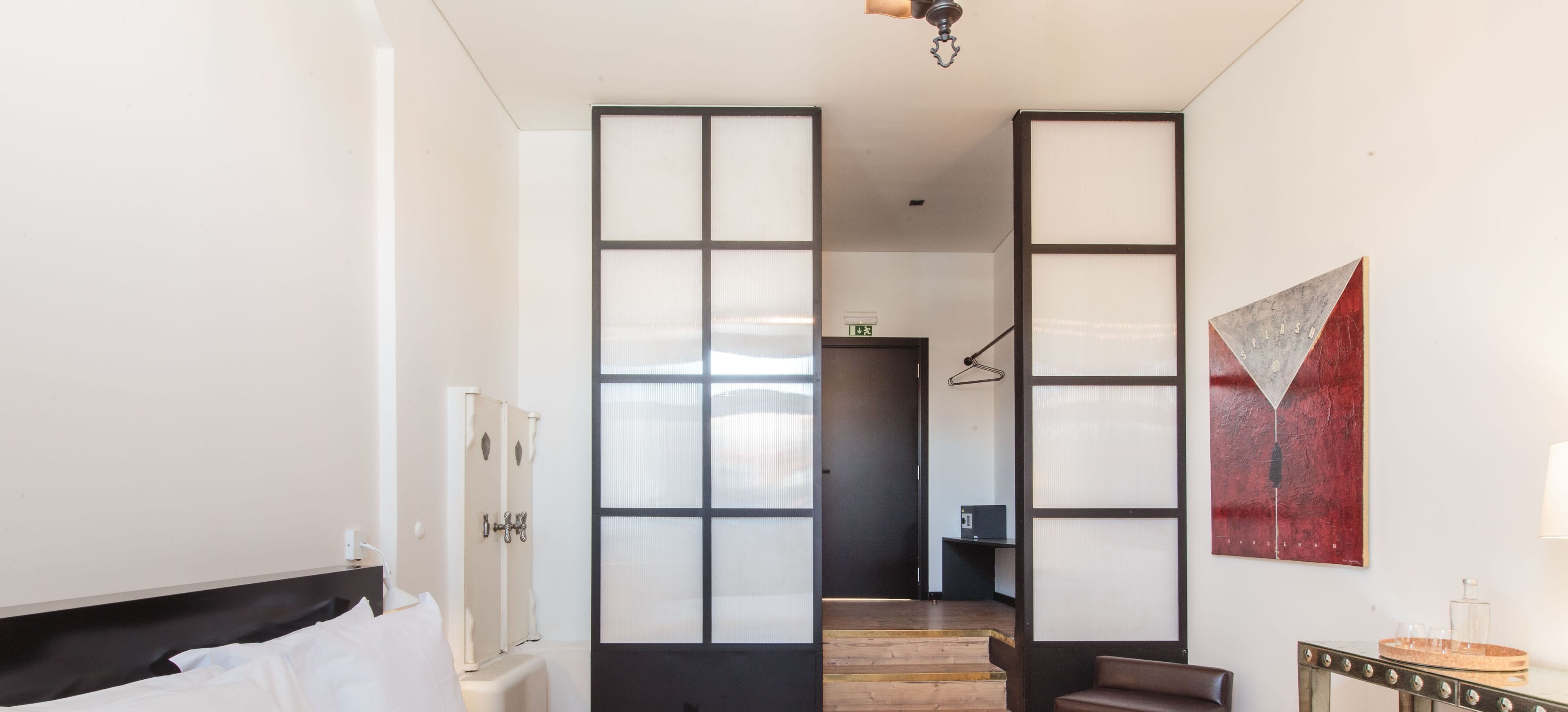 Habitación de hotel con cama, escritorio, silla, armario y un cuadro en la pared.
