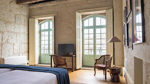 Un dormitorio con una cama, un escritorio, una silla y una lámpara. Hay dos ventanas con persianas verdes.