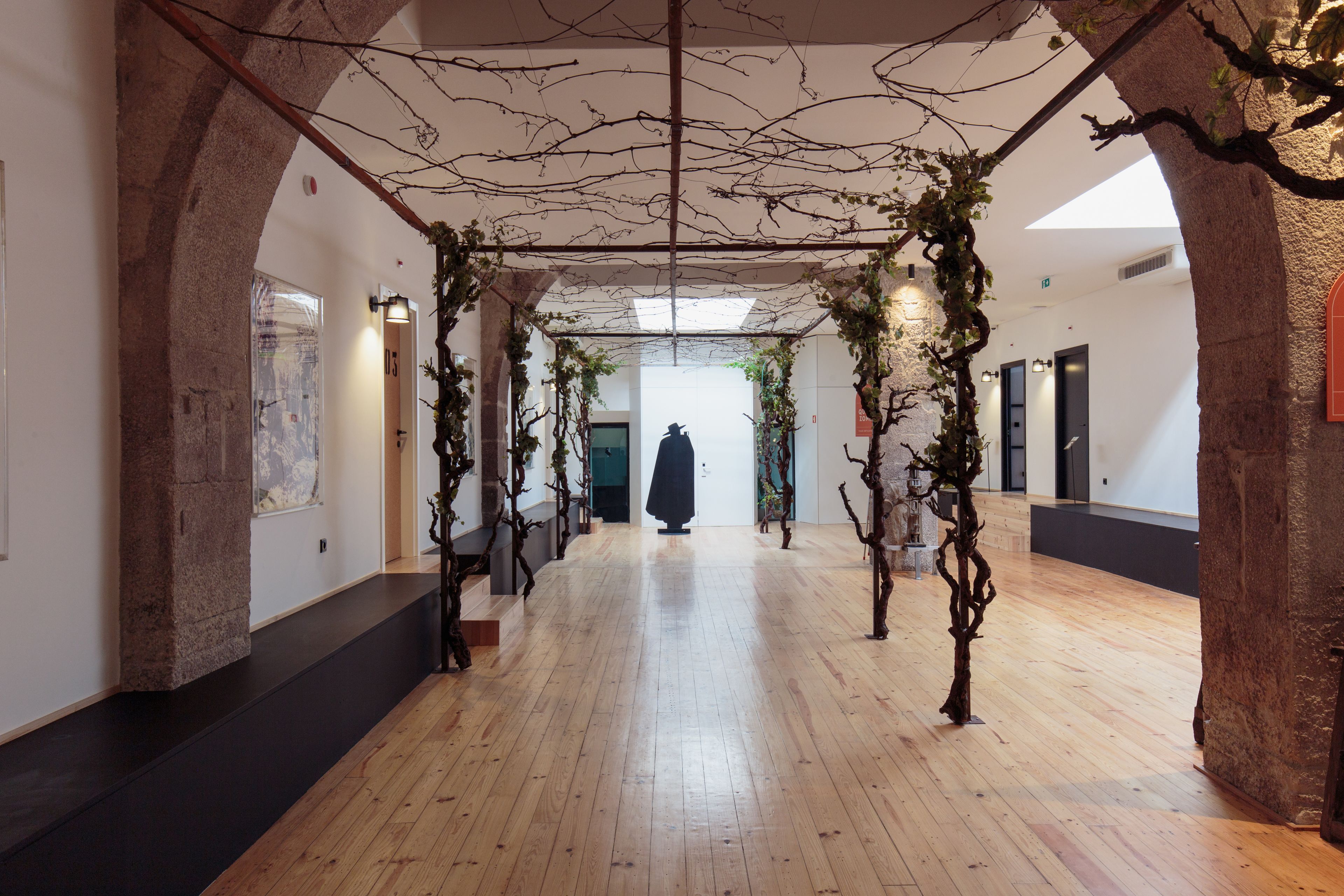 A hallway with wooden floors, stone arches, and hanging branches.