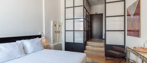 A hotel room with a large bed, a desk, a chair, and a staircase leading to another room.