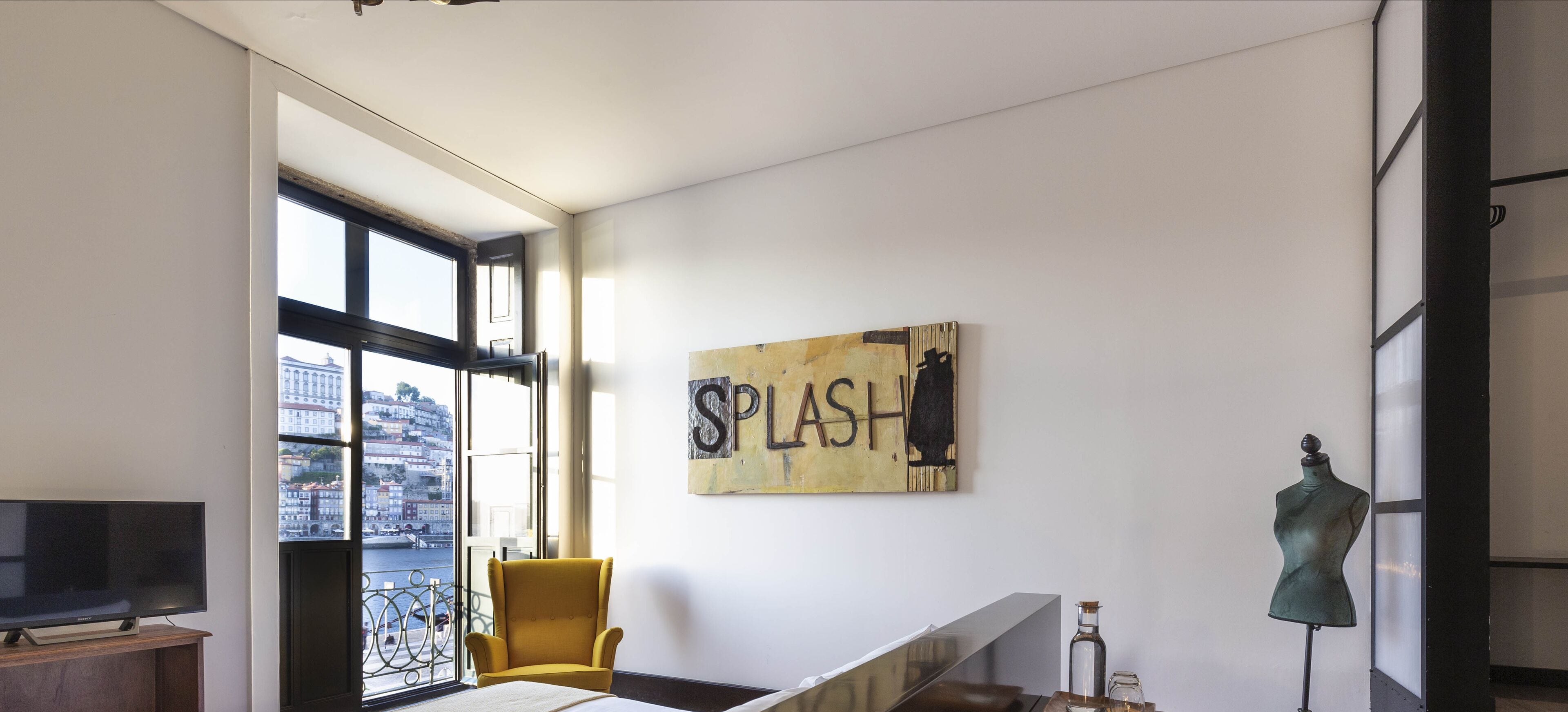 Una habitación moderna con un ventanal grande, un sillón amarillo, un televisor, una obra de arte en la pared y un maniquí.
