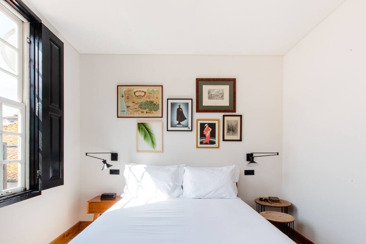 Une chambre à coucher comprenant un lit, deux tables de chevet, une fenêtre et des œuvres d’art accrochées au mur.