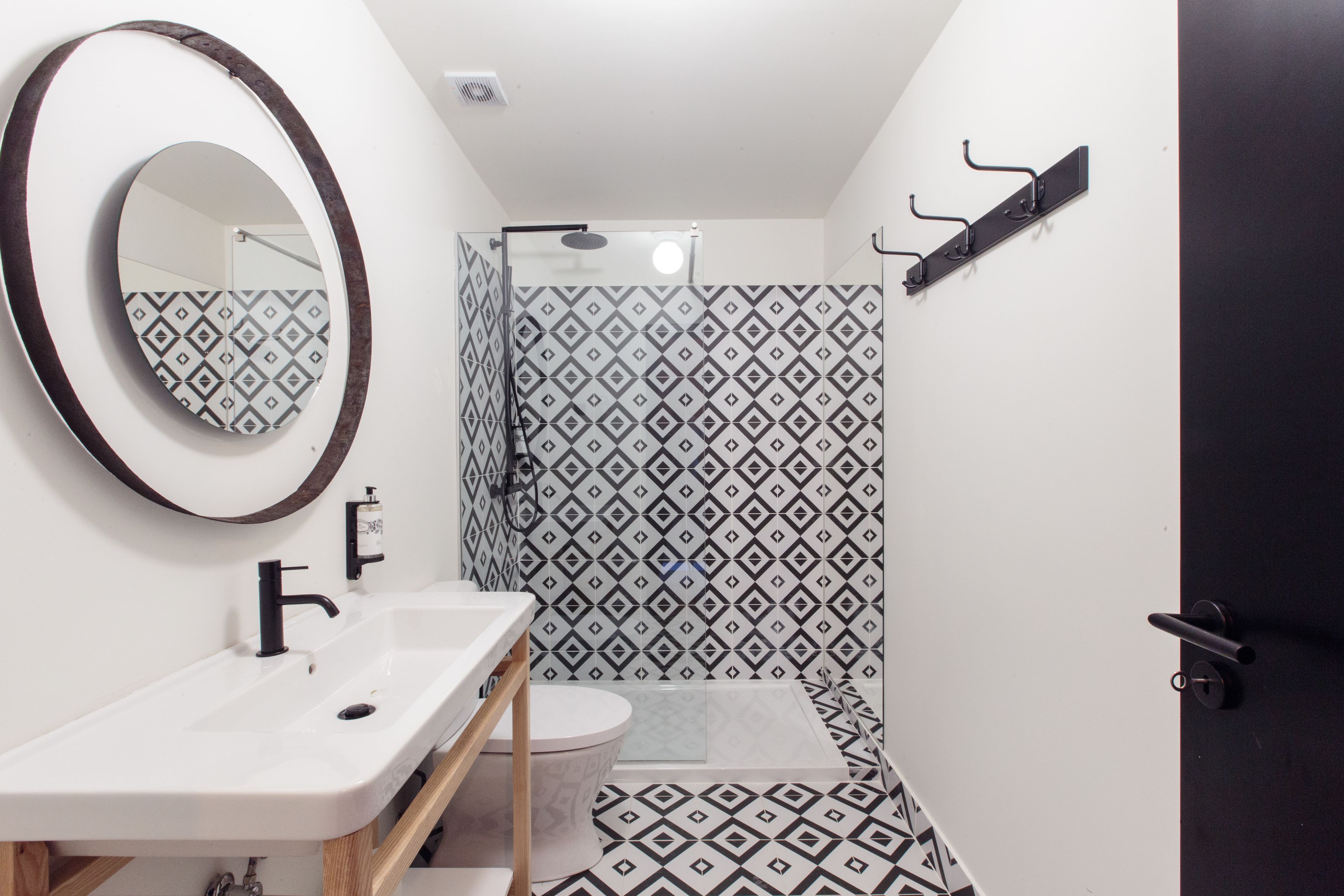 A bathroom with a white sink, a mirror, a shower with patterned tiles, and a door.