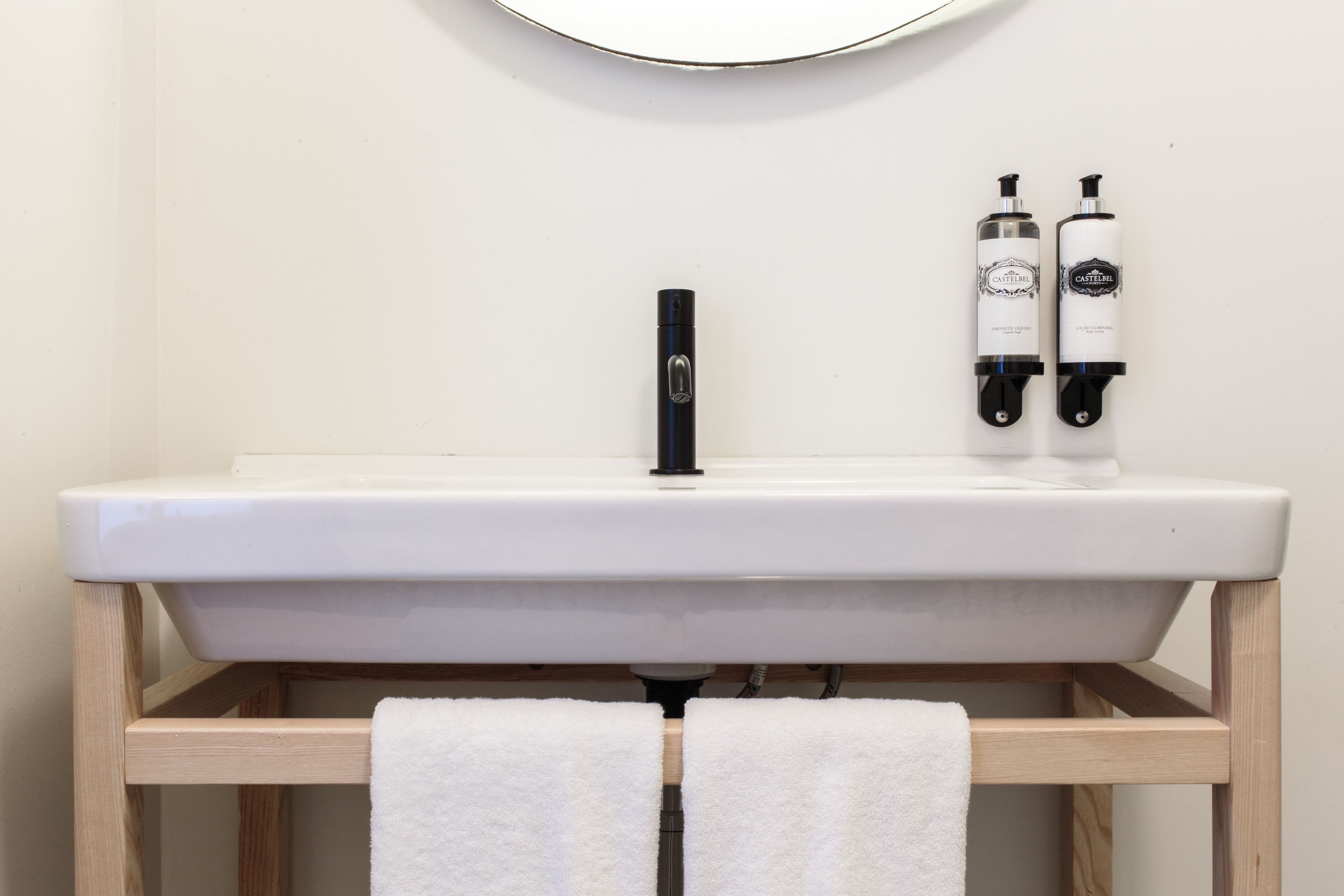 A bathroom with a white sink, two bottles of Castellar soap, and two white towels hanging from a wooden towel rack.