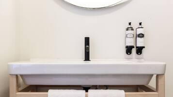 A bathroom with a white sink, two bottles of Castellar soap, and two white towels hanging from a wooden towel rack.