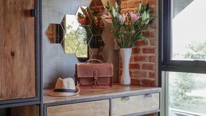 Una habitación con un armario de madera, un espejo, un florero con flores y una ventana con vistas.