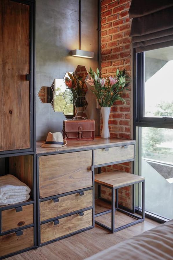 Una habitación con un armario de madera, un espejo, un florero con flores y una ventana con vistas.