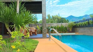 Piscina con plataforma de hormigón, rodeada de vegetación y vistas a montañas.