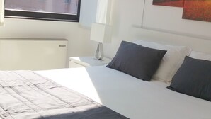 A bedroom with a large bed, a window with a view of a building, and a wall with three paintings. - Residence Nizza - Torino (Turin)
