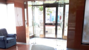 A hotel lobby with a blue chair, a glass door entrance, and a tiled floor. - Residence Nizza - Torino (Turin)