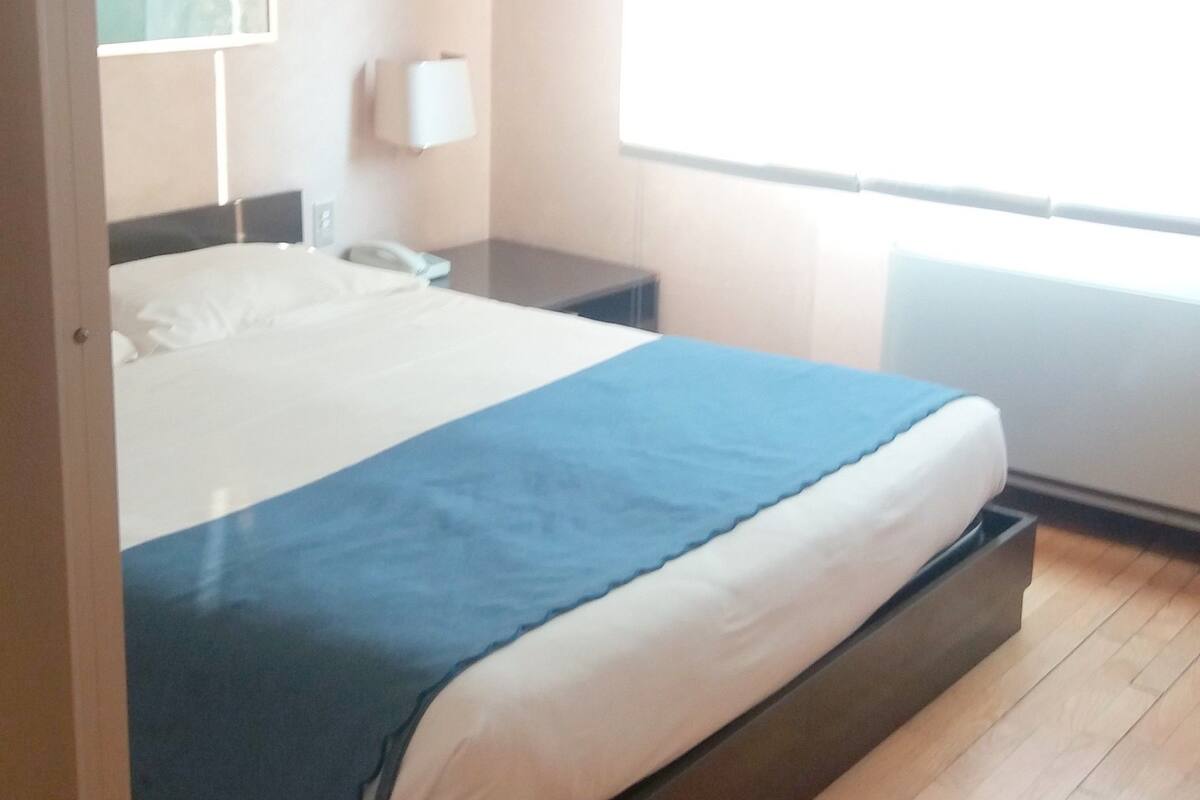 A bedroom with a bed, bedside table, lamp, and window.