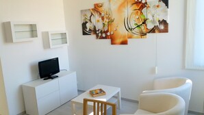 A modern living room with a flat-screen TV, a white sofa, a small table, and a decorative orchid painting. - Residence Nizza - Torino (Turin)