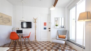 A modern room with a patterned floor, a television, a desk with chairs, a lamp, and a window with a view. - Welcome to Ruzafa Oasis by Florit Flats (Valencia)