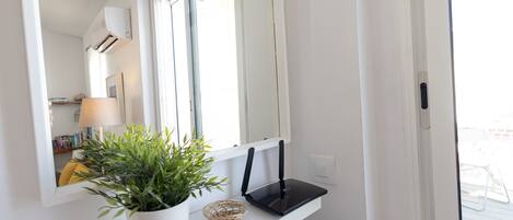 A white shelf with a potted plant, a basket, and a black device.