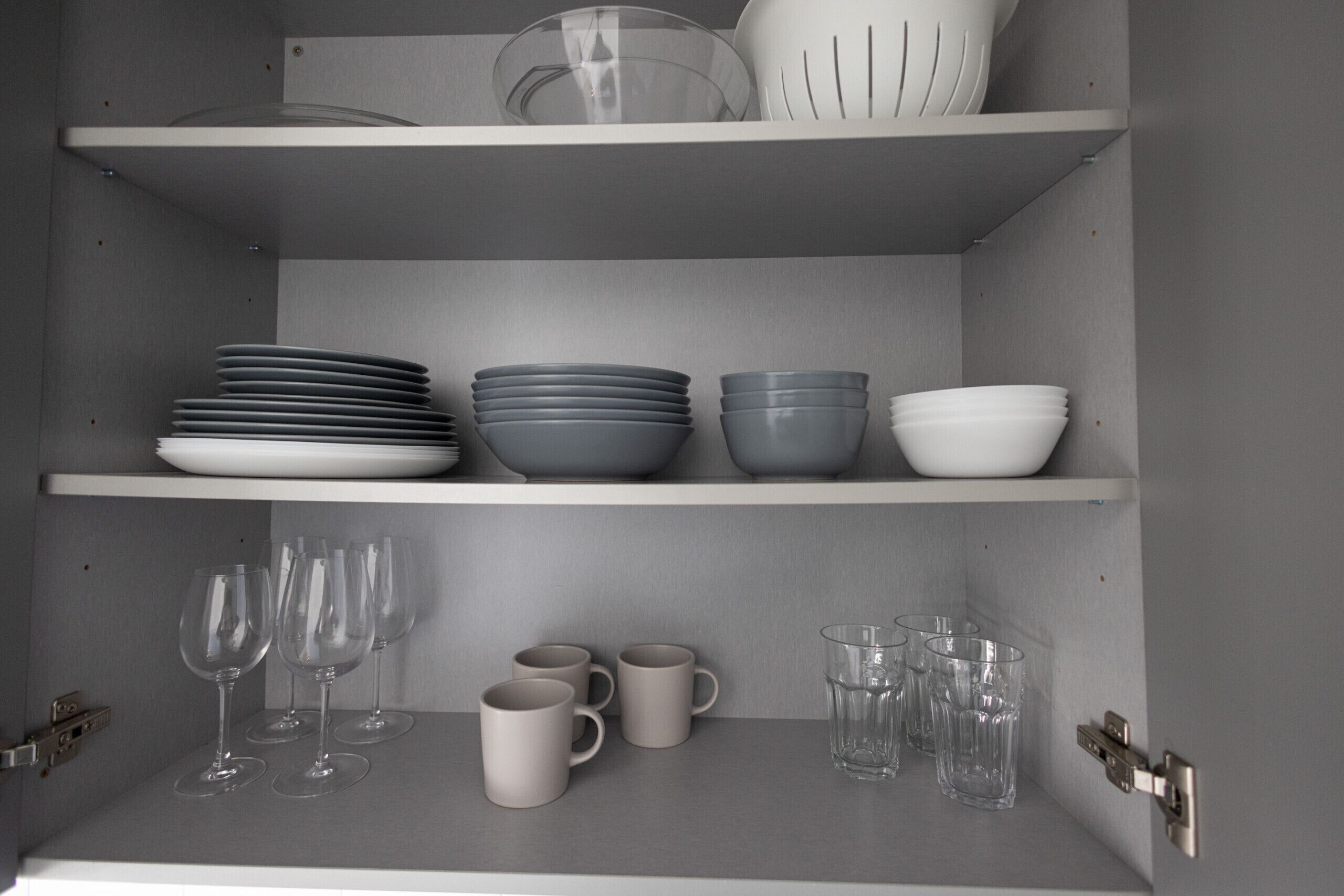A kitchen cabinet with shelves holding plates, bowls, mugs, and wine glasses.