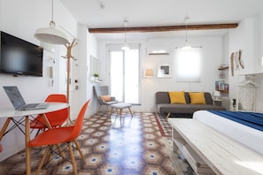 A modern room with a bed, a desk with a laptop, orange chairs, a gray sofa, and a patterned floor. - Welcome to Ruzafa Oasis by Florit Flats (Valencia)