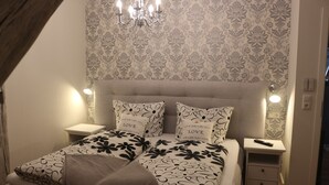 A bedroom with a bed, nightstands, a chandelier, and patterned wallpaper. - Holiday loft on the water with cathedral view DG (Hansestadt Havelberg)