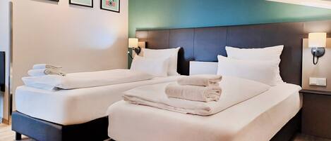 Ein Hotelzimmer mit zwei Betten, einer Türkis-farbenen Akzentwand und Wandlampen.