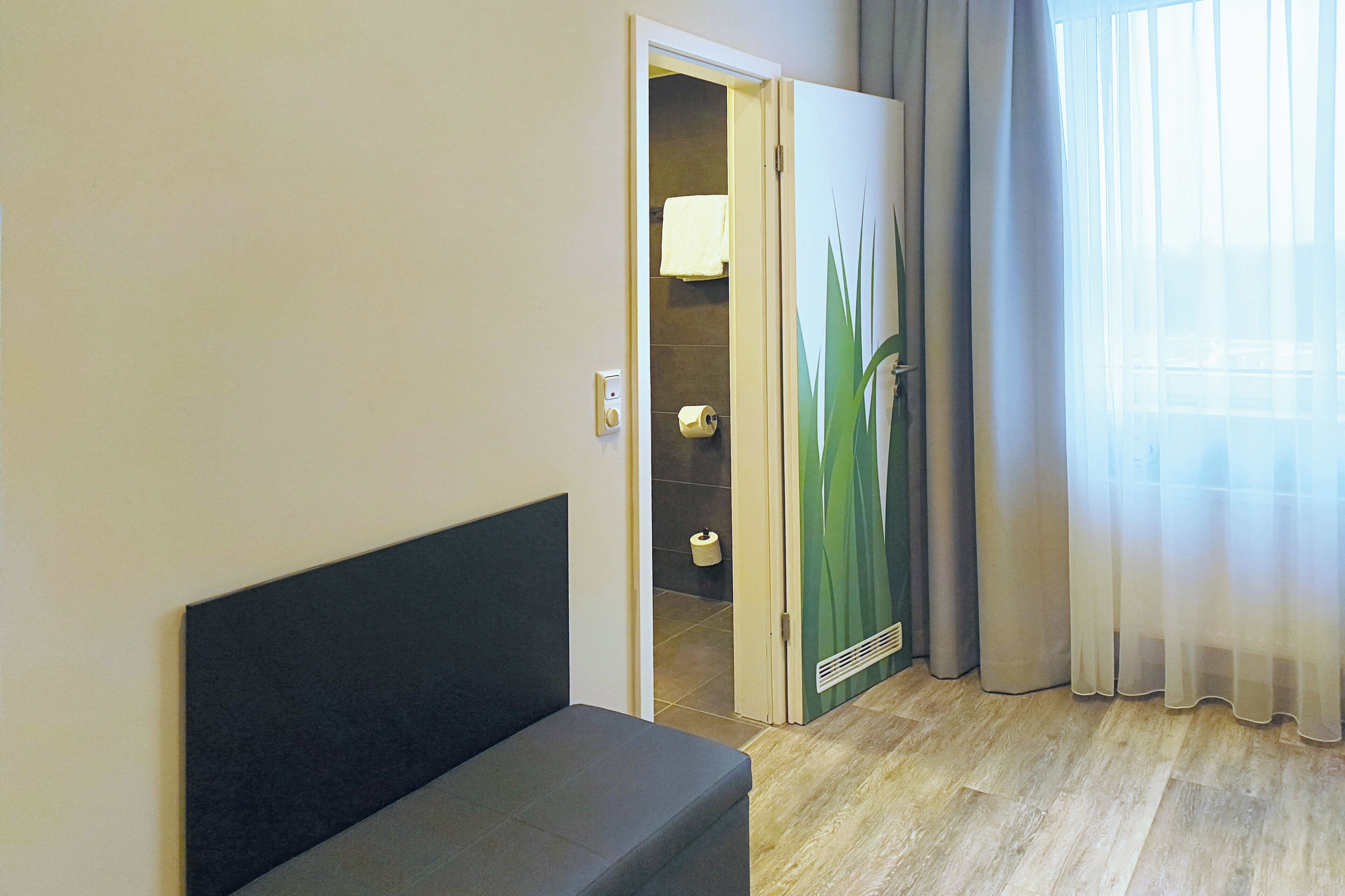 Quarto de hotel com cama, banheiro com toalha e janela com cortinas.