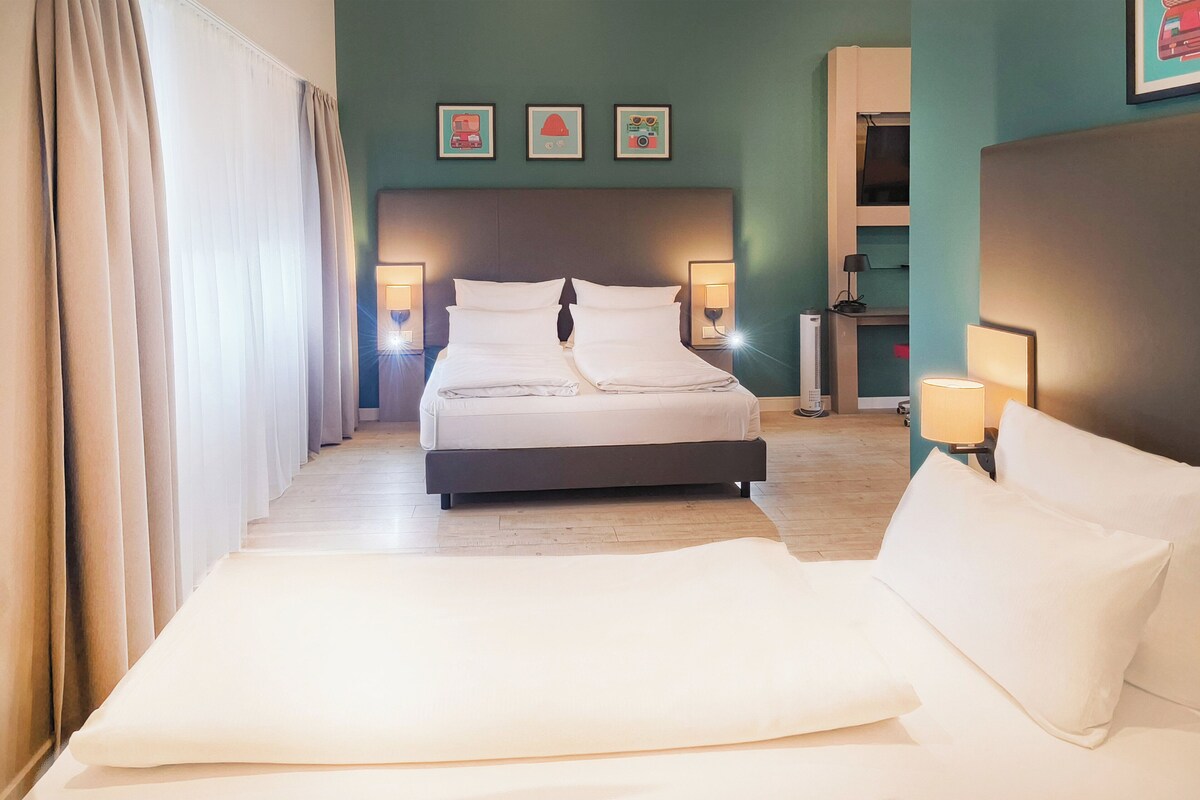 A hotel room with a bed, bedside lamps, a headboard, and a wall with three framed pictures.