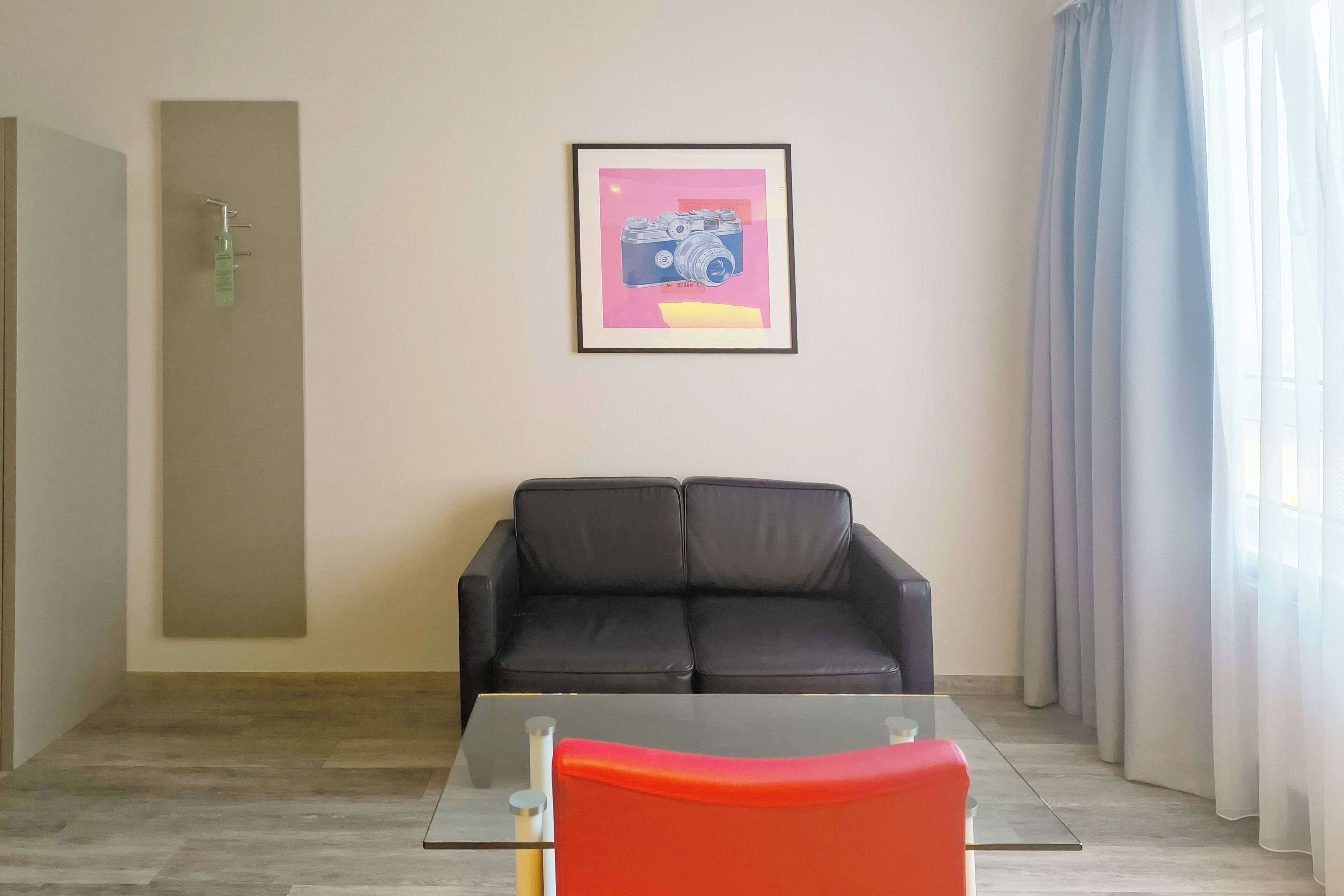 Ein modernes Zimmer mit einem Glastisch, einer schwarzen Ledersofa und einem gerahmten Foto einer Kamera an der Wand.