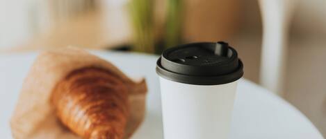 A croissant and a coffee cup on a white plate.