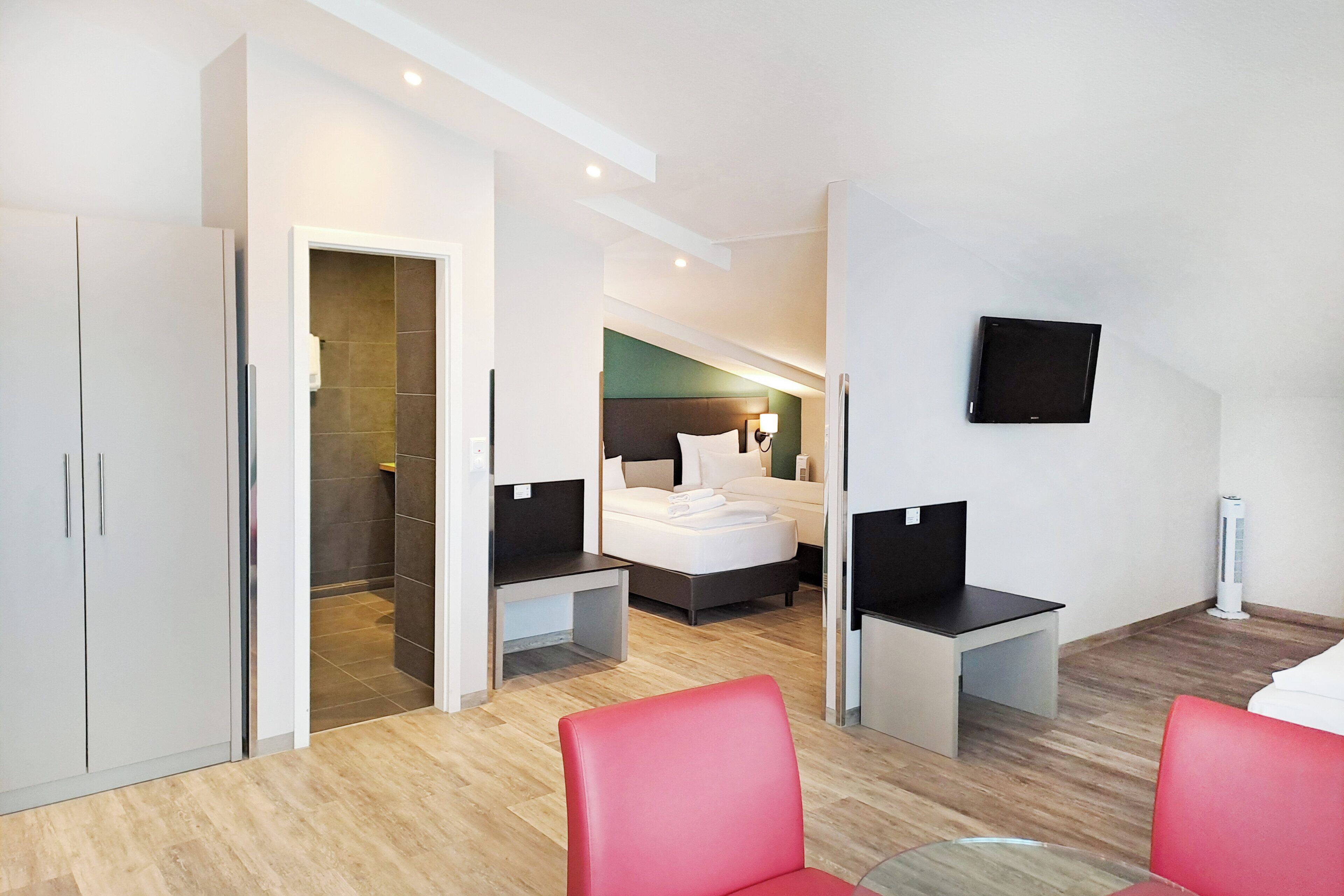 A modern hotel room with a bed, a desk, a chair, and a TV.