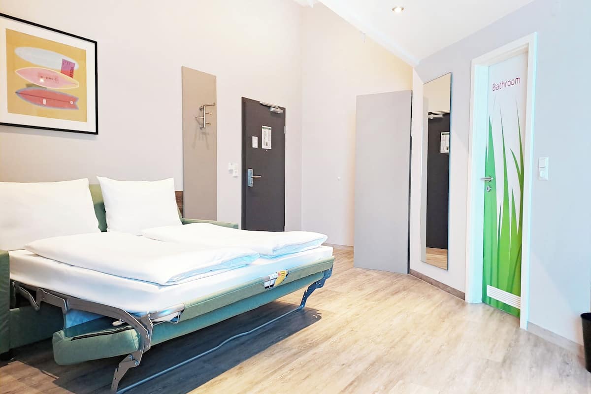 Quarto de hotel com cama, porta de banheiro e espelho.