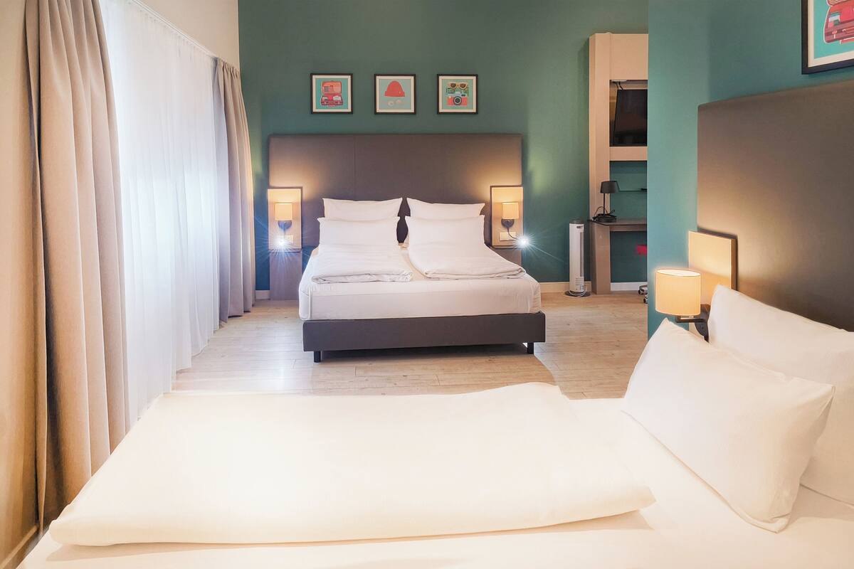 Una habitación de hotel con una cama, lámparas de noche, un cabecero y una pared con tres cuadros.