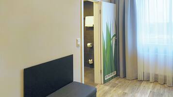 A hotel room with a bed, a bathroom with a towel, and a window with curtains.