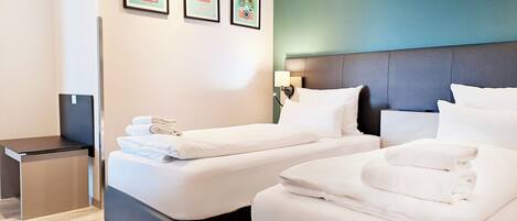A hotel room with two beds, a small desk, and a wall with framed pictures.