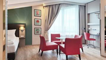 A hotel room with a bed, a desk, a chair, a table, and a window with curtains.