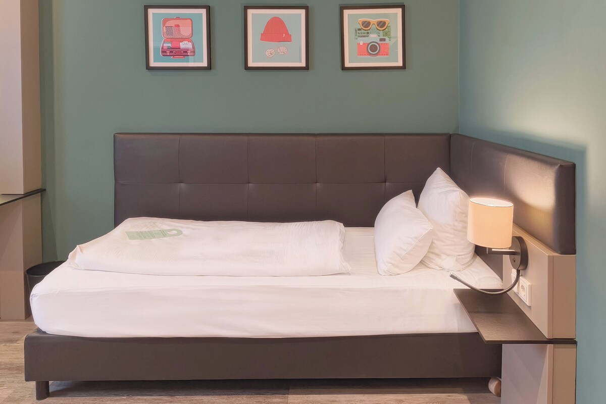 A neatly made bed with a headboard, a bedside lamp, and three framed pictures on the wall.