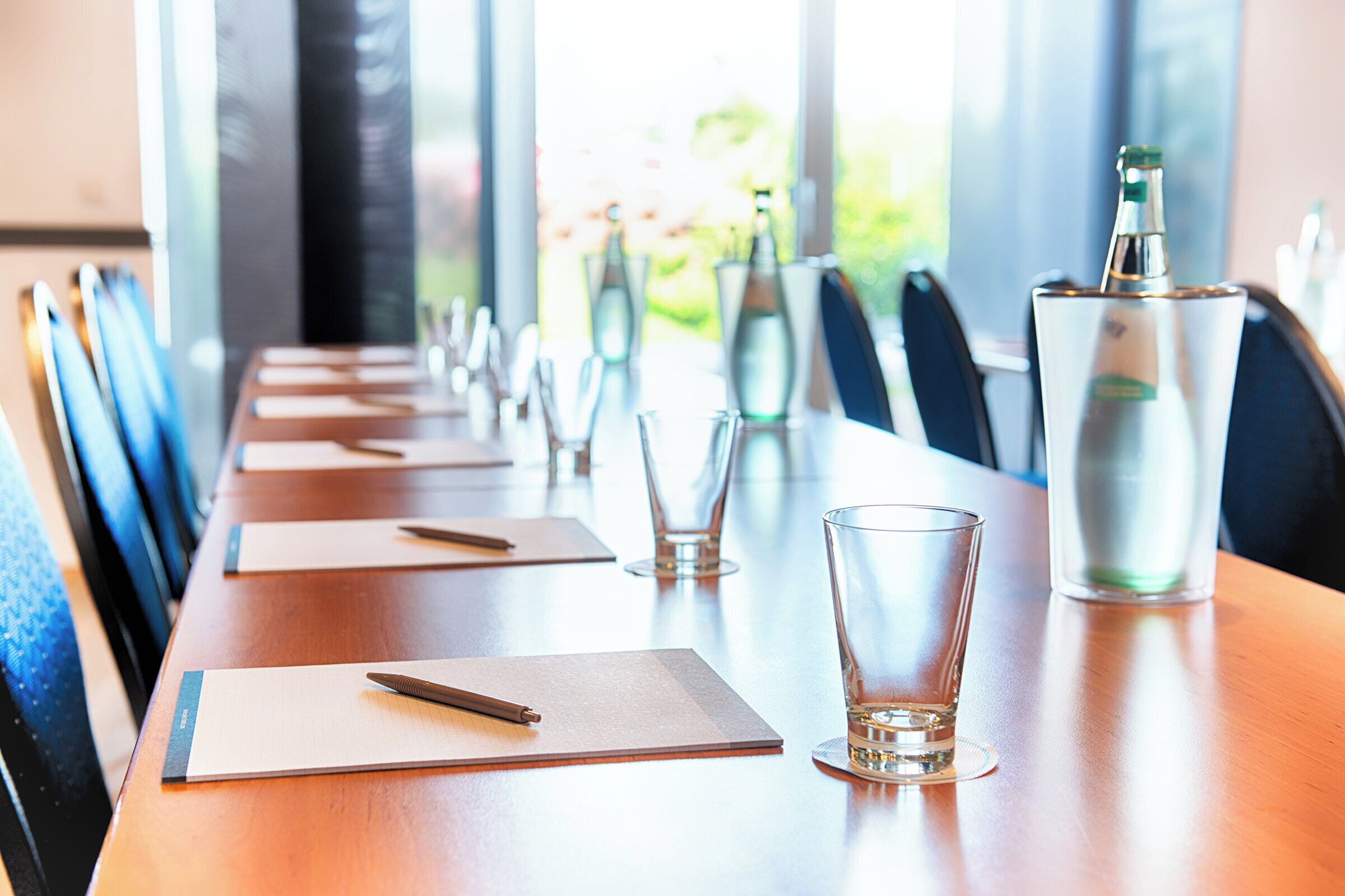 A conference table with chairs, water glasses, and a bottle.