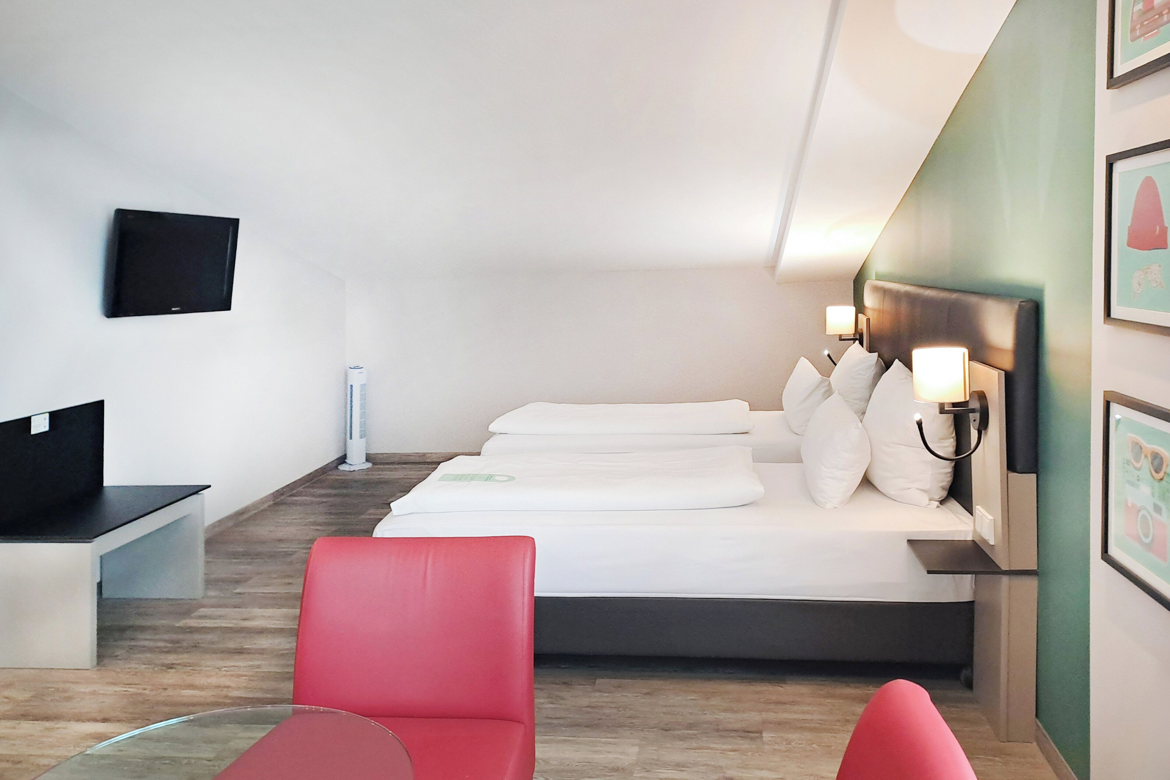 Quarto de hotel com uma cama, uma escrivaninha, uma cadeira e uma televisão.