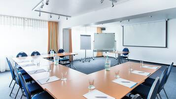 Ein Konferenzraum mit langem Tisch, Stühlen, einer Whiteboard und einer Projektionsleinwand.