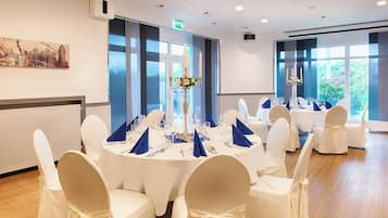 Une salle de conférence avec des tables rondes, des chaises blanches et de grandes fenêtres.
