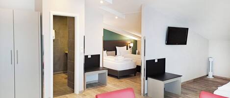 A modern hotel room with a bed, a desk, a chair, a TV, and a wardrobe.