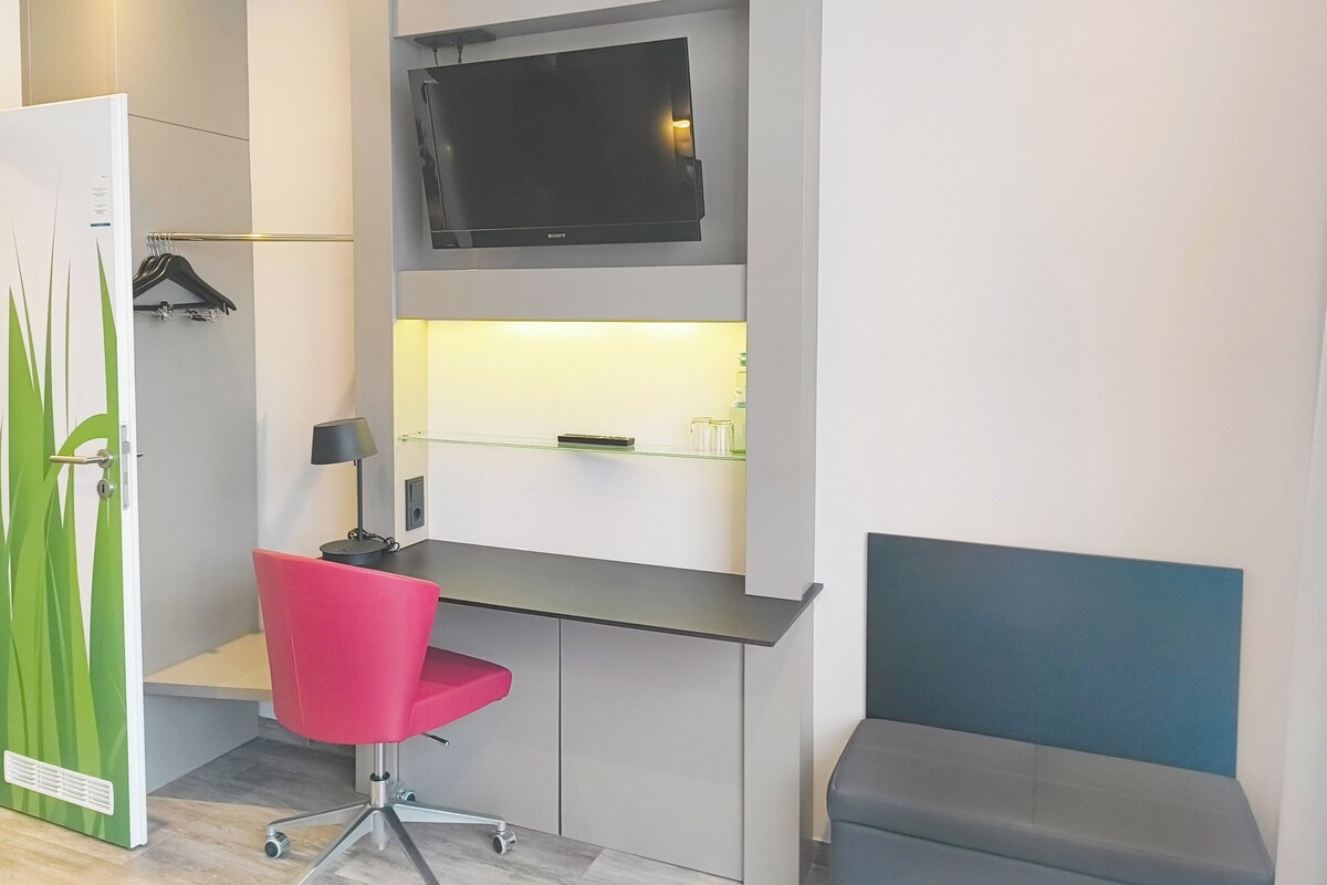 A modern room with a desk, a flat-screen TV, a red chair, a bench, and a green door.