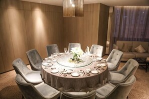 Una mesa redonda de comedor con ocho sillas, una araña y un sofá al fondo.