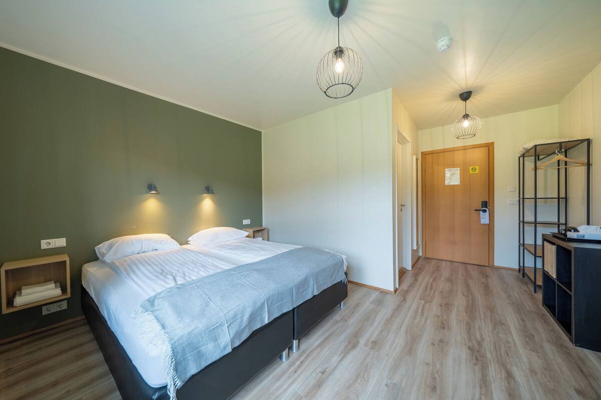 Un dormitorio moderno con una cama grande, lámparas de noche, un armario de madera y un escritorio con un perchero.